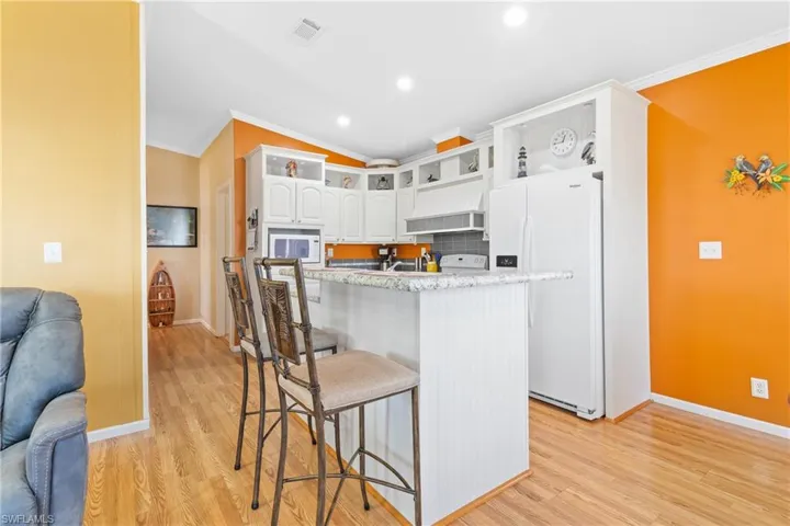 Kitchen with white cabinets, a breakfast bar area, ornamental molding, light stone counters, and white appliances