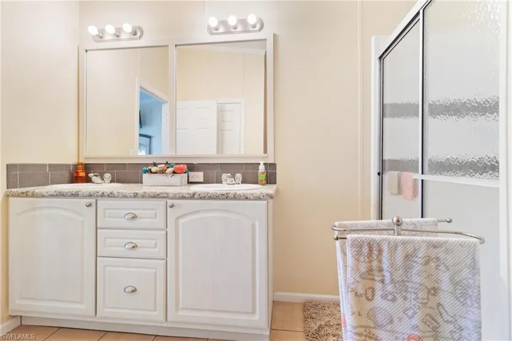 Bathroom with vanity, tile patterned floors, decorative backsplash, and a shower with door