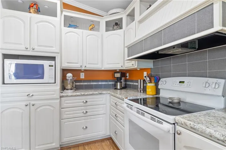 Kitchen with white cabinetry, custom range hood, and white appliances