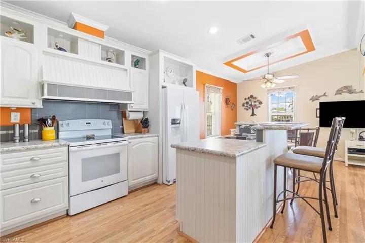 Kitchen featuring light hardwood / wood-style flooring, an island with sink, white cabinetry, and white appliances