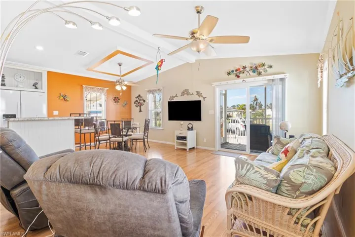 Living room with lofted ceiling with beams, ceiling fan, light wood-type flooring, and a wealth of natural light