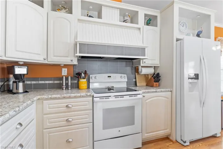 Kitchen featuring white appliances, light wood-type flooring, backsplash, white cabinets, and light stone counters