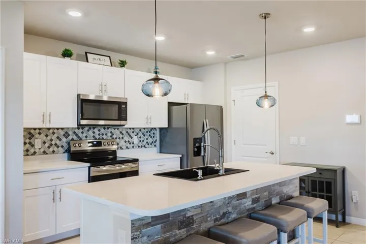 Contemporary kitchen featuring white cabinetry, stainless steel appliances, a mosaic tile backsplash, and an island with a stone veneer facade