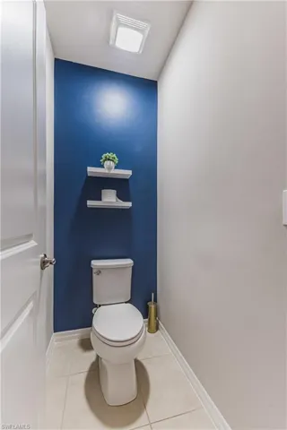White toilet with a rectangular tank, two white floating shelves, and tile flooring
