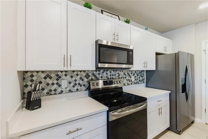 White shaker-style cabinetry, mosaic tile backsplash, stainless steel microwave, stainless steel range, and stainless steel refrigerator