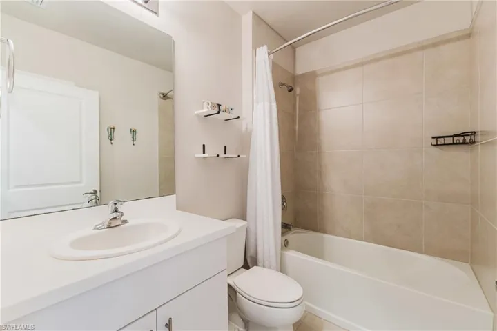 Bathroom featuring a single vanity with an integrated sink, a large wall-mounted mirror, a toilet, and a bathtub with a shower head and tiled surround