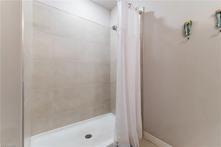 Shower stall featuring large format neutral-toned wall tiles and a white shower pan