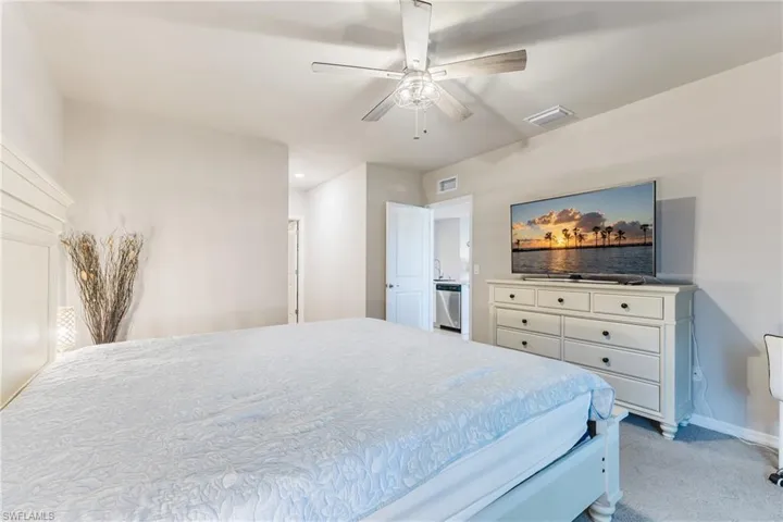 Neutral wall tones with carpeted flooring, featuring a ceiling fan with integrated lighting, and an open doorway revealing a partial built-in appliance