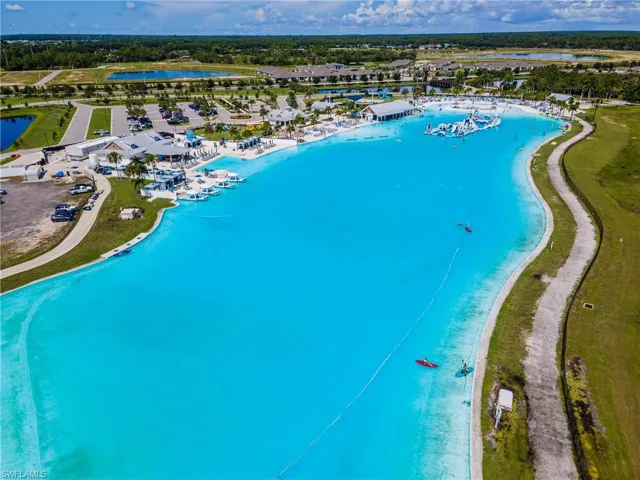 Expansive artificial lagoon with bright blue water, surrounded by a paved walking path, green landscaping, and multiple resort-style buildings
