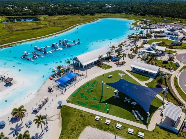 Expansive lagoon with water obstacle course, sandy shore, multiple shade structures, miniature golf course, and surrounding green spaces