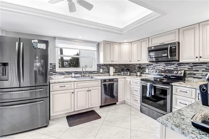 Kitchen with stainless steel appliances, light stone countertops, light marble finish flooring, decorative backsplash, and crown molding