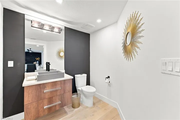 Floating wood-finish vanity with a vessel sink and matte black faucet, illuminated by a three-light fixture
