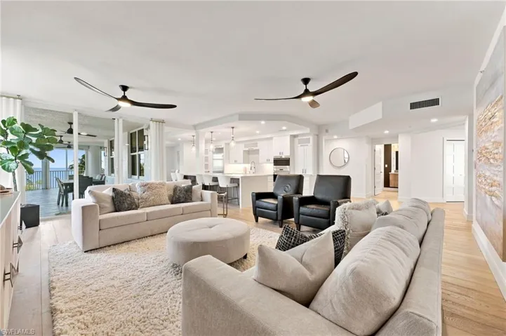 Open-concept living space with light-tone wood flooring, recessed lighting, and a white kitchen featuring a breakfast bar
