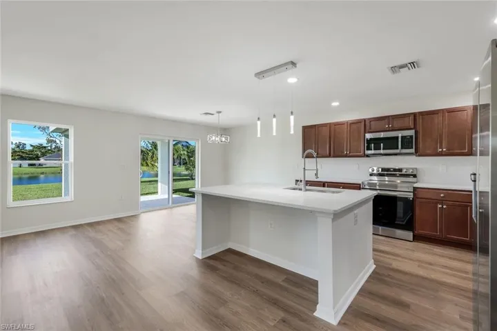 Kitchen featuring appliances with stainless steel finishes, pendant lighting, hardwood / wood-style flooring, and a center island with sink
