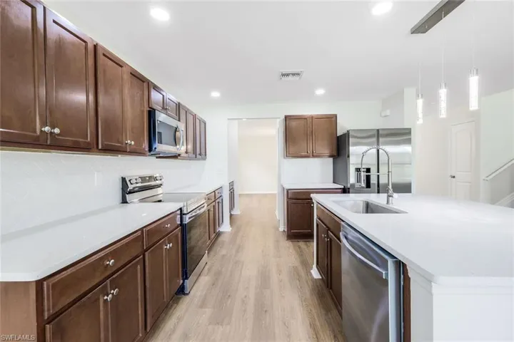 Kitchen featuring an island with sink, stainless steel appliances, light hardwood / wood-style floors, decorative backsplash, and decorative light fixtures