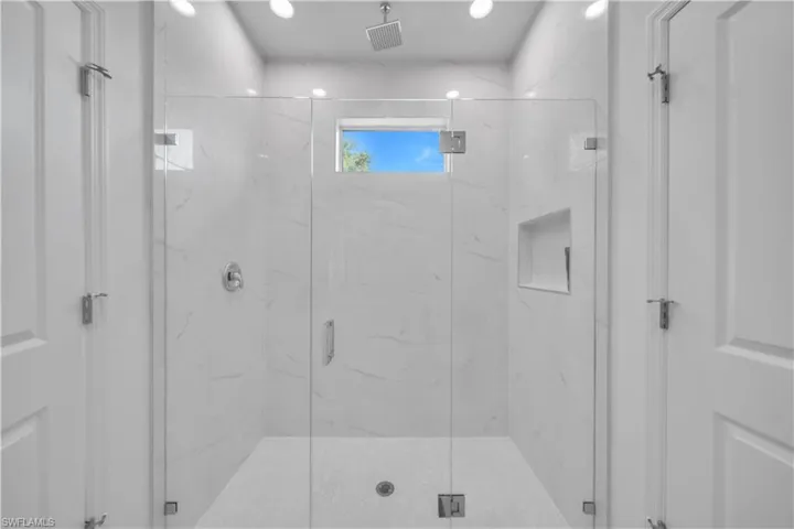 Frameless glass shower enclosure featuring white marble-patterned tile, a rainfall showerhead, and a built-in shower niche