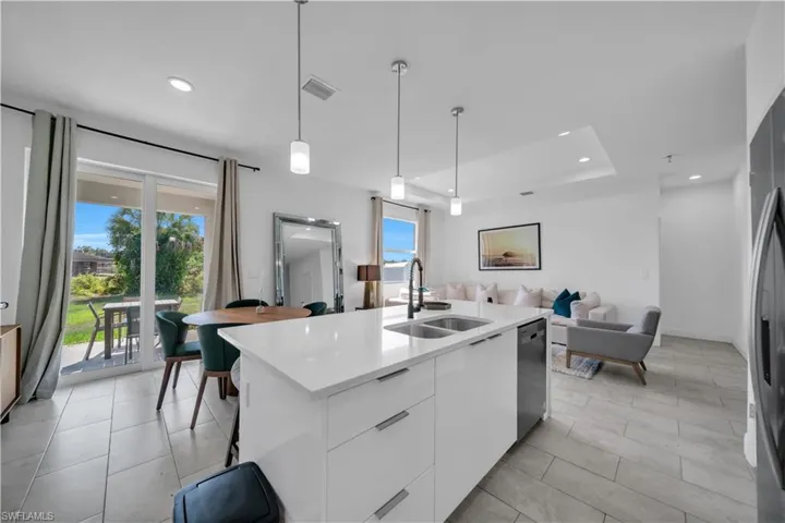 Open-concept living space featuring a kitchen island with dual sinks, a stainless steel dishwasher, and pendant lighting