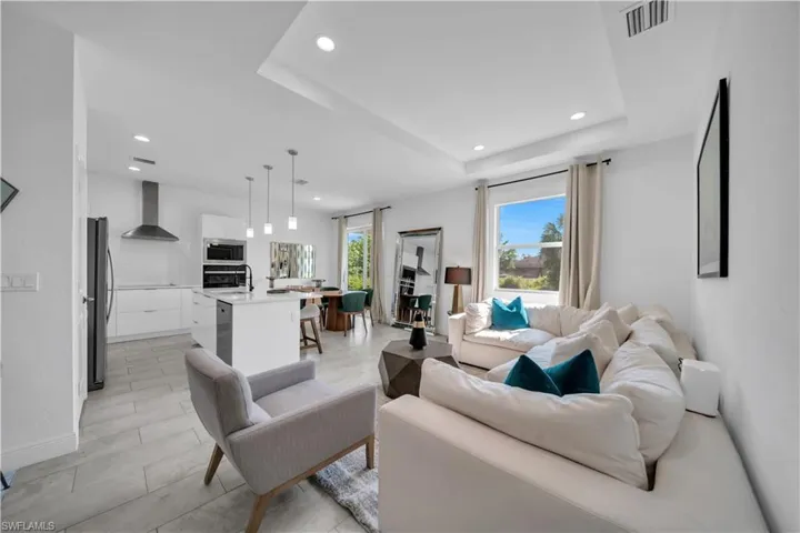 Open-concept living area featuring light-toned tile flooring, recessed lighting, and a tray ceiling