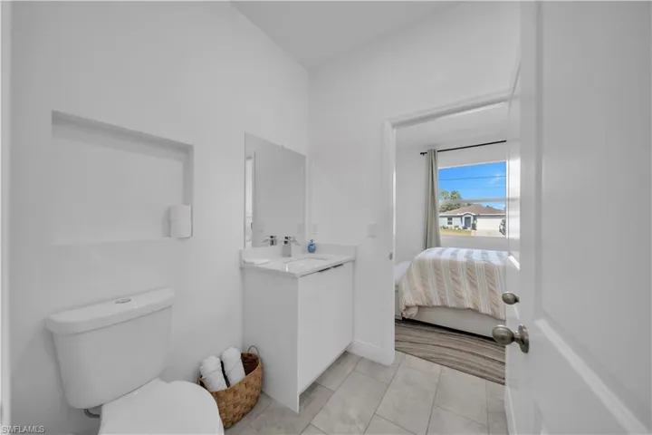 Bathroom featuring a built-in wall niche, white vanity with integrated sink, rectangular mirror, and light-toned tile flooring