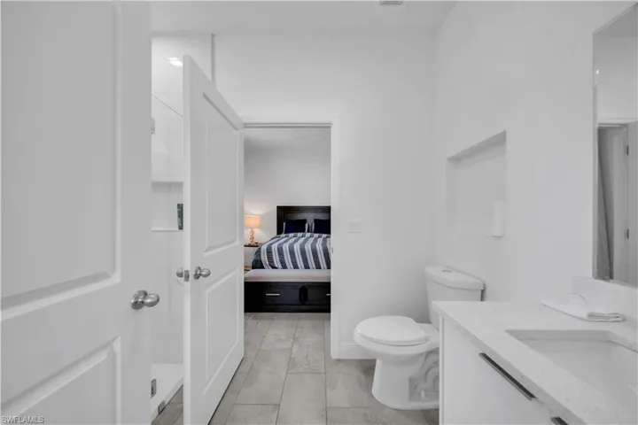 Bathroom featuring a white vanity with an undermount sink and light-colored countertop, a toilet, a recessed wall niche, and tile flooring