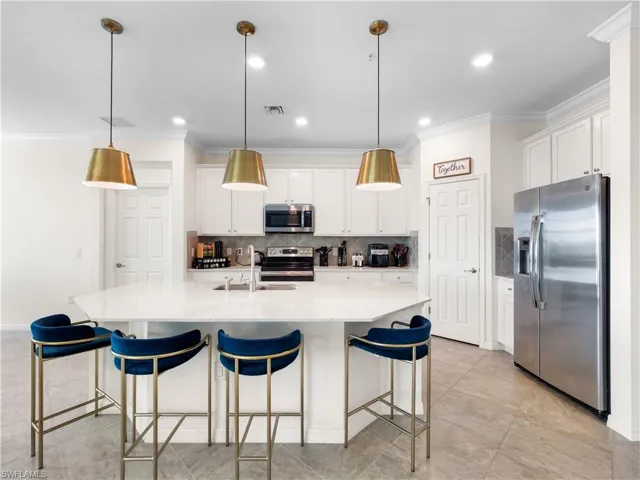 Kitchen featuring stainless steel appliances, a kitchen breakfast bar, crown molding, an island with sink, and white cabinets
