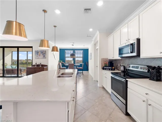 Kitchen featuring stainless steel appliances, white cabinetry, a kitchen island with sink, light stone countertops, and tasteful backsplash