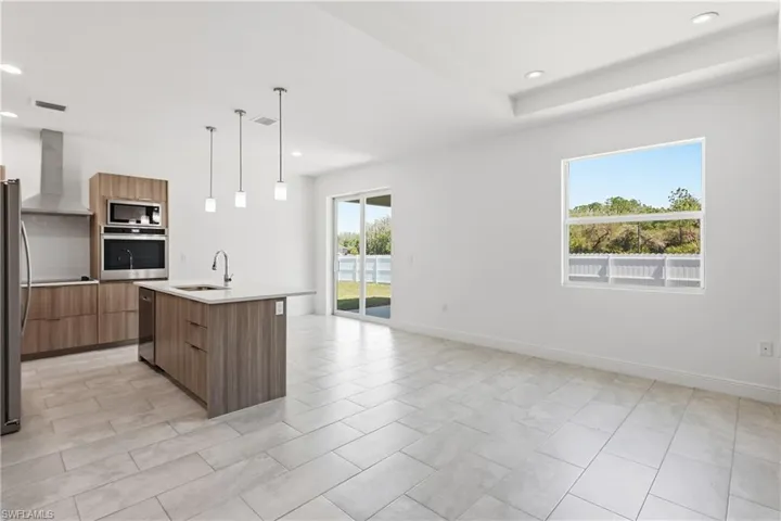 Kitchen featuring modern cabinets, stainless steel appliances, a center island with sink, and hanging light fixtures