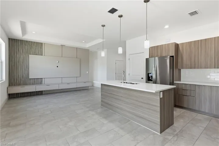 Kitchen featuring modern cabinets, an island with sink, wood finish cabinets, stainless steel refrigerator with ice dispenser, and a tray ceiling