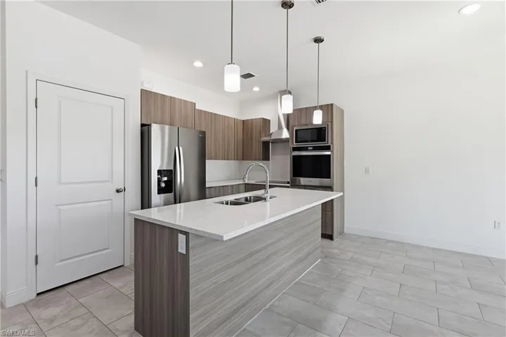 Kitchen with modern cabinets, a kitchen island with sink, stainless steel appliances, light stone countertops, and hanging light fixtures