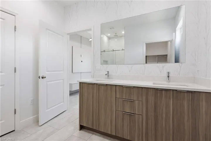 Full bathroom with double vanity and a marble finish shower