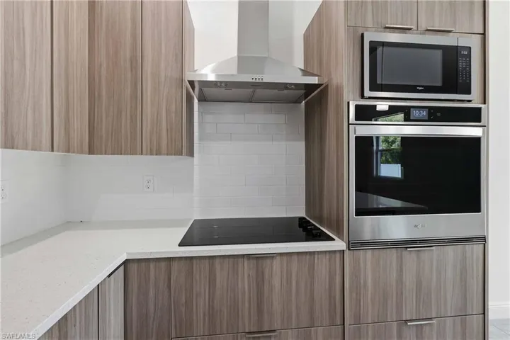 Kitchen with modern cabinets, stainless steel appliances, light stone countertops, and backsplash