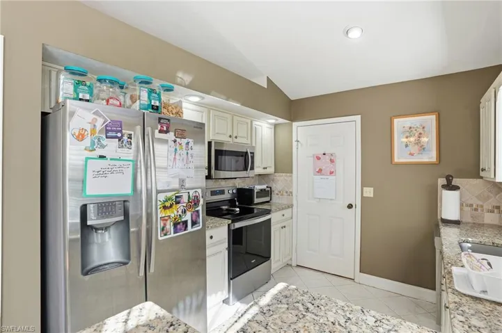 Kitchen with stainless steel appliances, tasteful backsplash, light tile patterned flooring, light stone countertops, and lofted ceiling