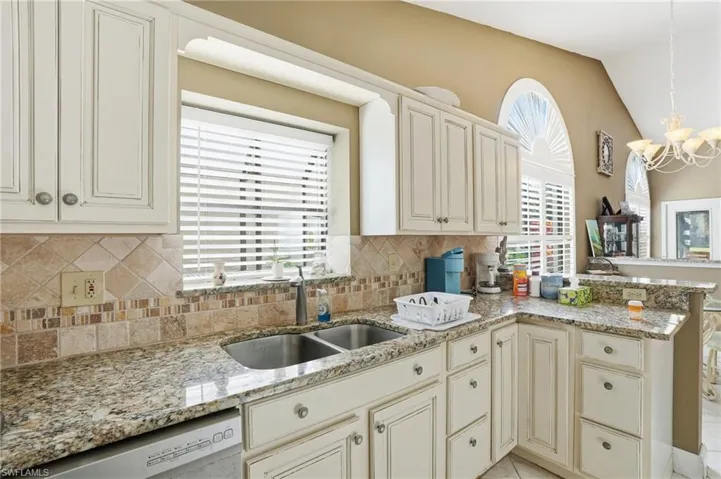 Kitchen with vaulted ceiling, light stone countertops, a peninsula, stainless steel dishwasher, and healthy amount of natural light