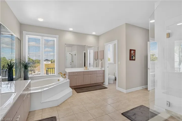 Bathroom with a shower stall, two vanities, a bath, light tile patterned flooring, and a bidet
