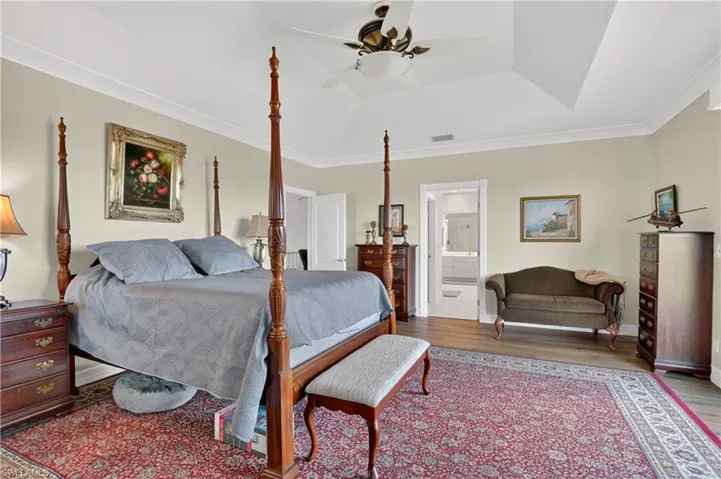Bedroom featuring crown molding, wood finished floors, a ceiling fan, a tray ceiling, and ensuite bathroom