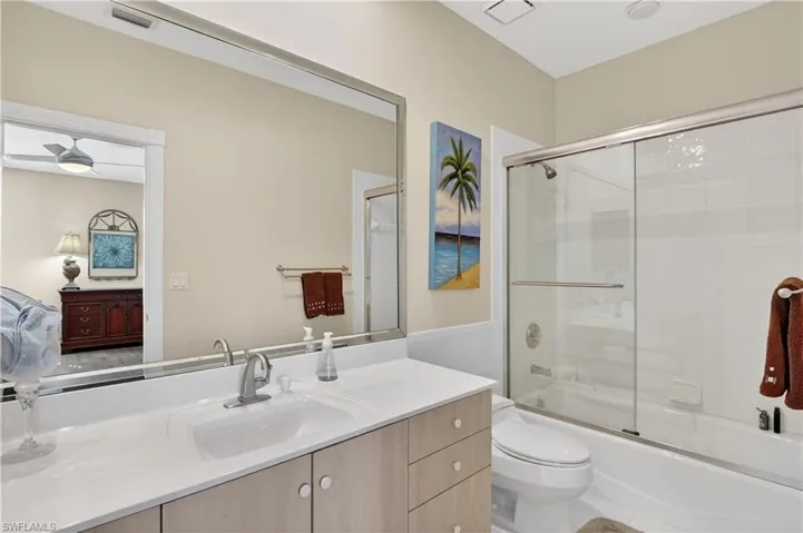 Bathroom featuring connected bathroom, combined bath / shower with glass door, vanity, and a wainscoted wall