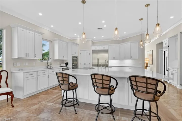 Kitchen with white cabinetry, appliances with stainless steel finishes, a breakfast bar area, a spacious island, and pendant lighting