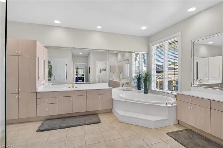 Full bathroom featuring two vanities, a garden tub, light tile patterned floors, and recessed lighting