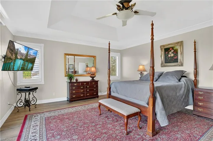 Bedroom with wood finished floors, a ceiling fan, a tray ceiling, and ornamental molding