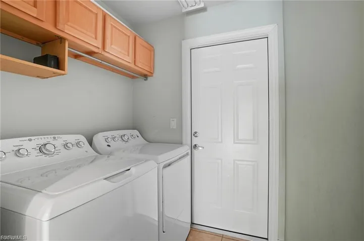 Laundry area with washing machine and clothes dryer, light tile patterned floors, and cabinet space