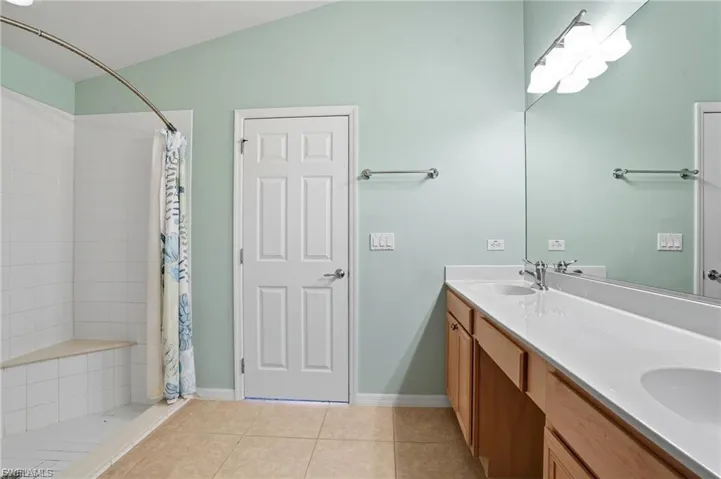 Full bath featuring a shower stall, light tile patterned floors, and double vanity