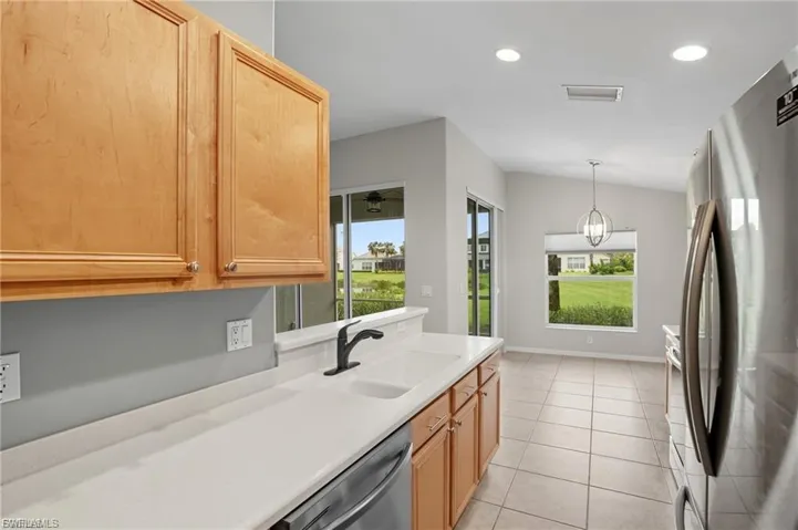 Kitchen featuring stainless steel appliances, light countertops, light wood finish cabinets, light tile patterned flooring, and decorative light fixtures