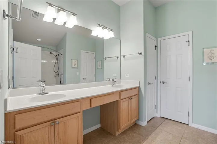 Bathroom featuring double vanity, light tile patterned floors, tiled shower, and a closet