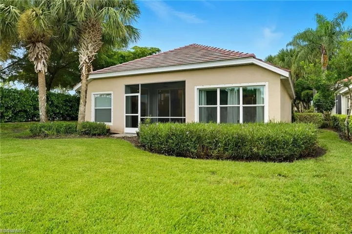Rear view of property featuring stucco siding, a lawn, a sunroom, and a tile roof