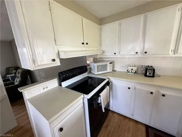 Kitchen with black range with electric stovetop, white cabinetry, white microwave, light countertops, and dark wood finished floors