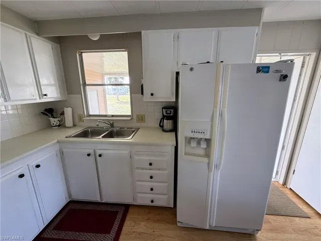 Kitchen with white fridge with ice dispenser, white cabinetry, light countertops, and decorative backsplash