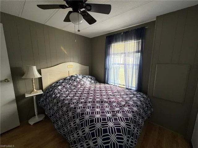 Bedroom featuring wooden walls, dark wood-style flooring, and ceiling fan
