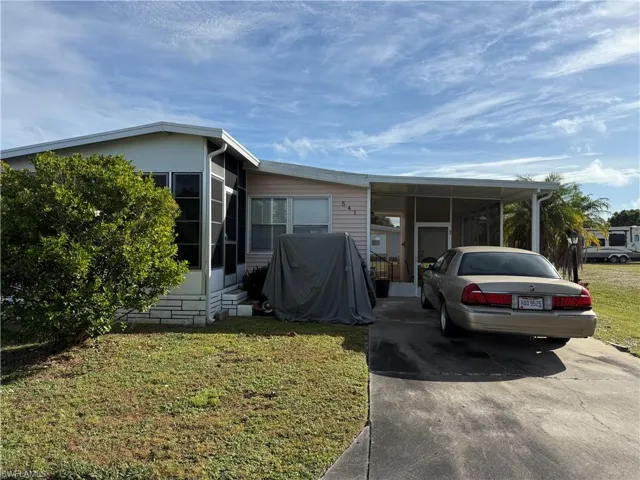 Manufactured / mobile home featuring a front yard, an attached carport, driveway, and a sunroom