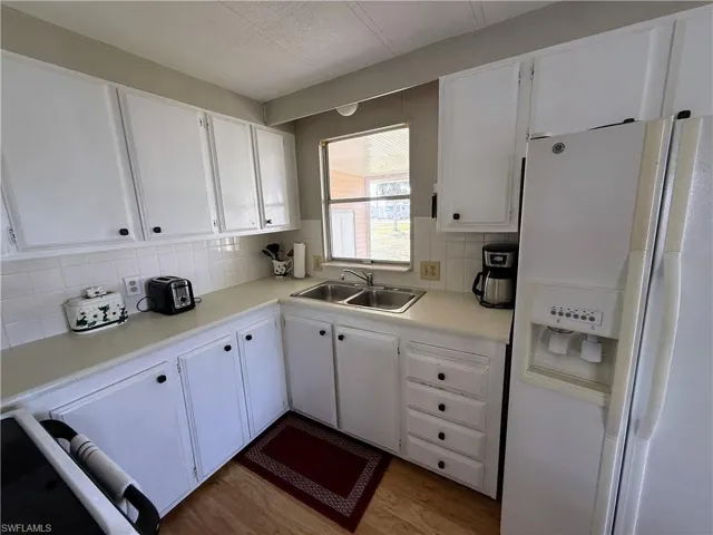 Kitchen with white refrigerator with ice dispenser, white cabinets, light countertops, tasteful backsplash, and light wood-style flooring