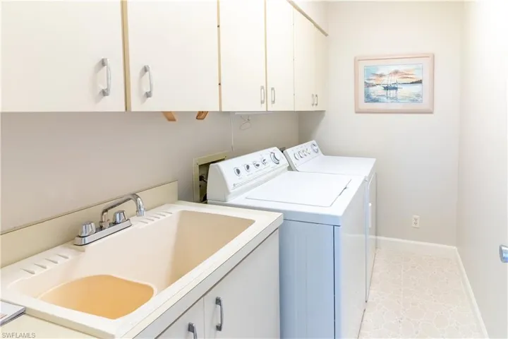 Clothes washing area featuring cabinets, separate washer and dryer, light tile patterned floors, and sink